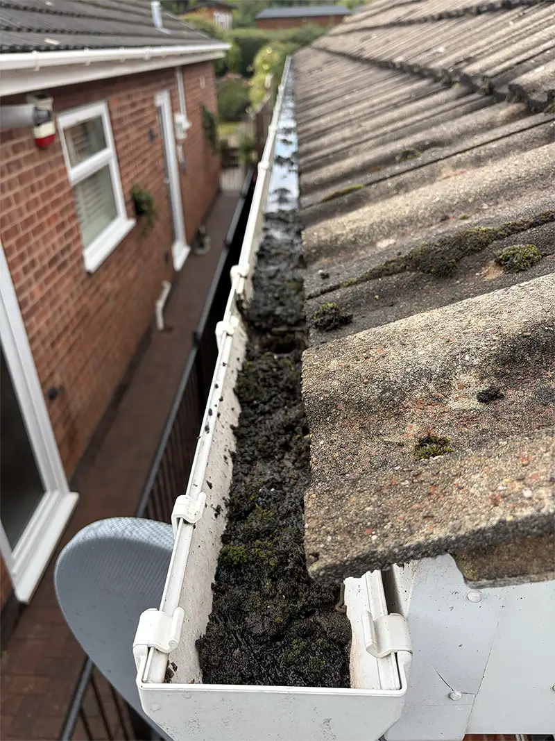 Blocked guttering filled with moss and debris before vacuum clearing